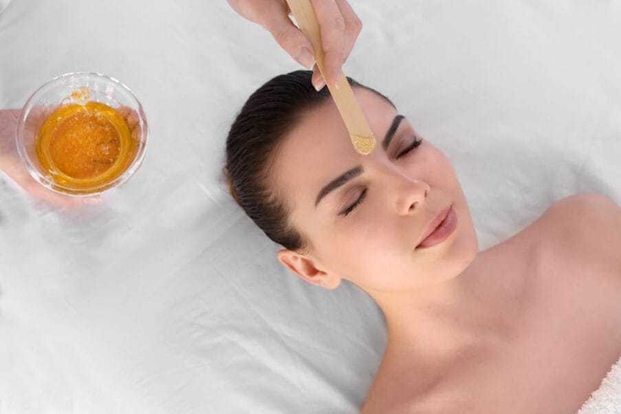 Woman receiving a facial honey treatment with wooden applicator in a spa.