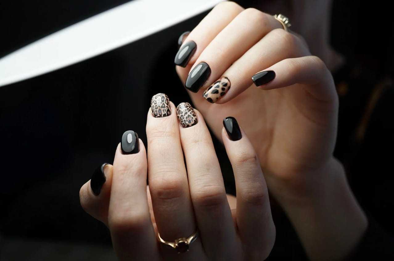 Stylish black manicure with leopard print accent nails.