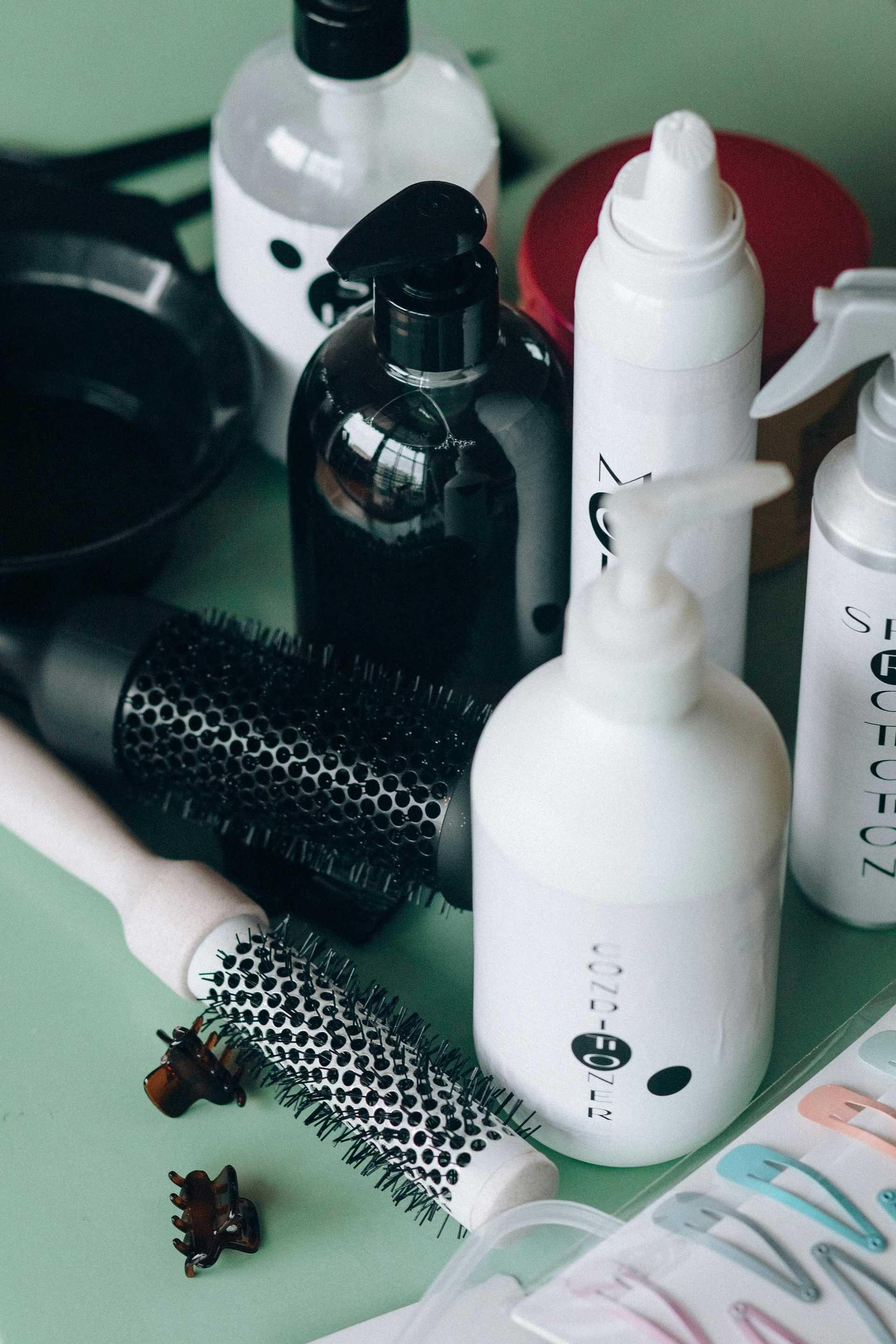 Assorted hairstyling products and tools on a green surface, including brushes and spray bottles.